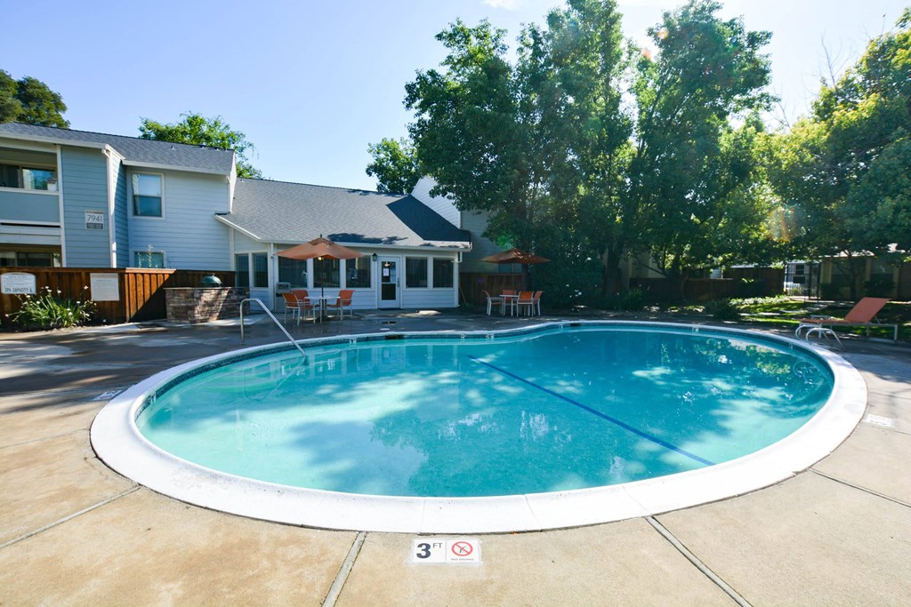 View of community pool, lush shrubbery, private patio/ balcony and exterior of buildings