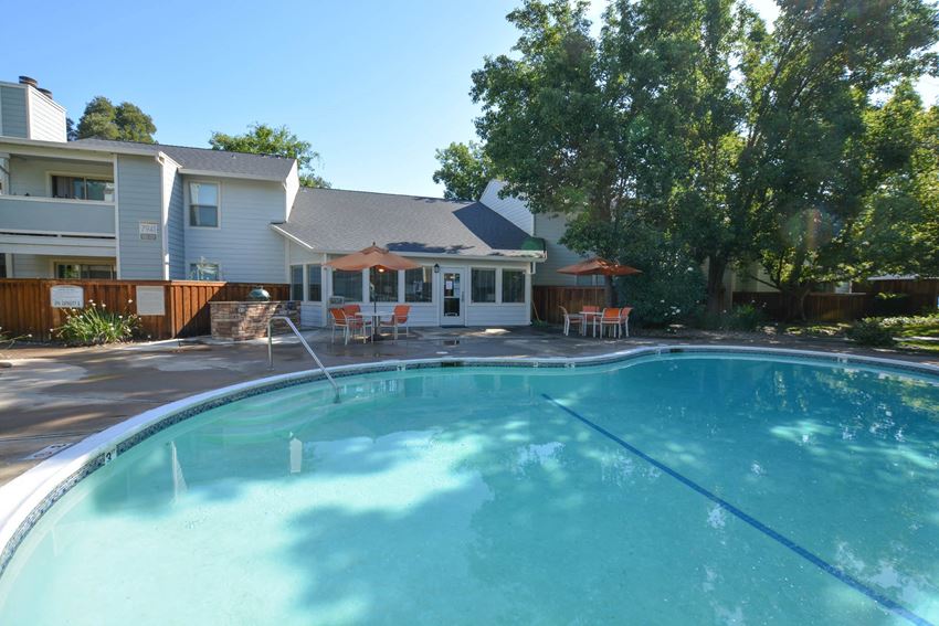 View of community pool and exterior of buildings, grilling stations, and sitting area with umbrellas and tables - Photo Gallery