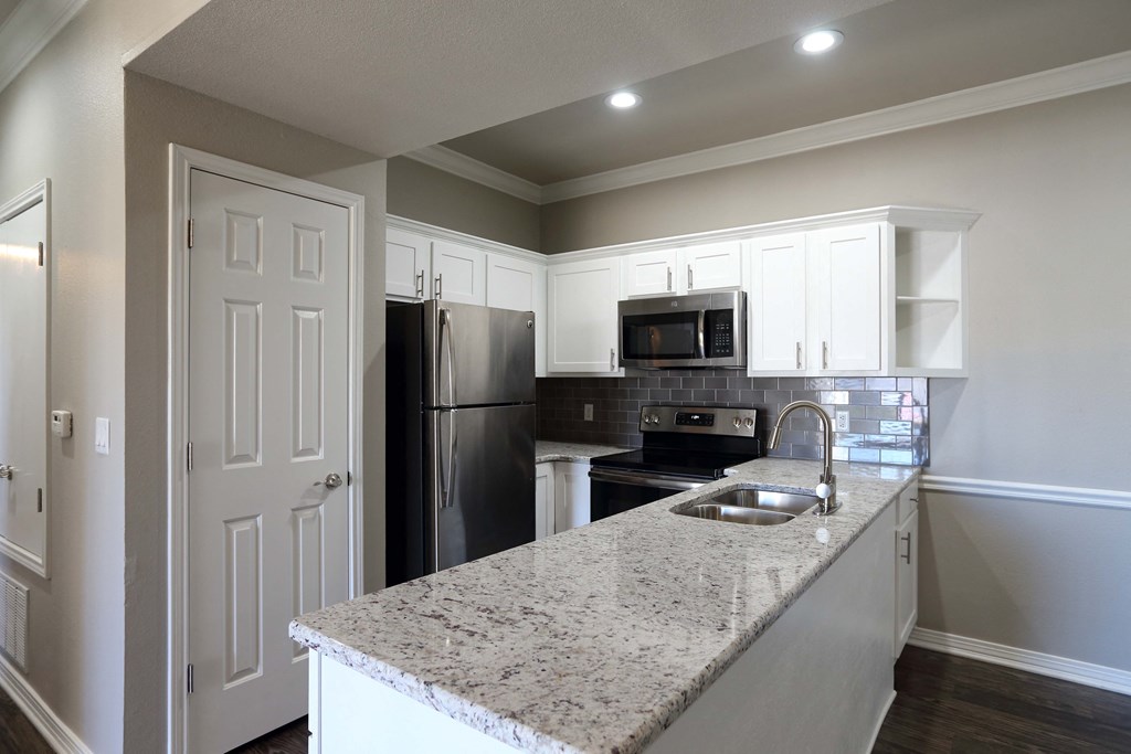 View of open kitchen area with wood look flooring, granite counters, tile backsplash, stainless appliances and recessed lighting.