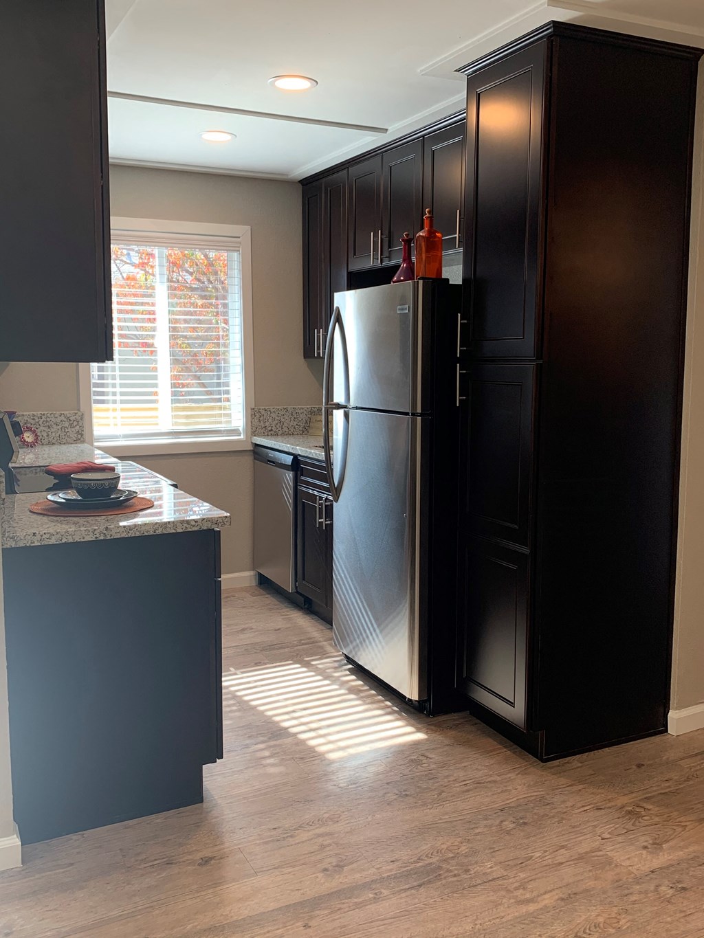 View of kitchen with brown cabinets, wood like flooring, stainless appliances, and well lit window in kitchen