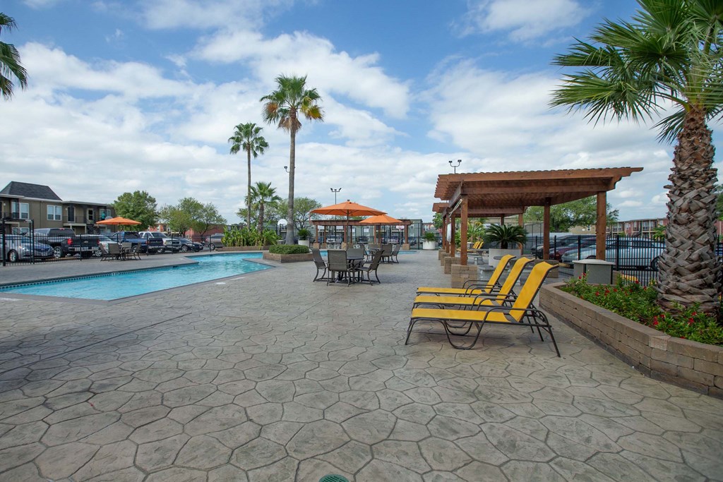A pool area with a patio, chairs and umbrellas at Willow Creek Apartments, Texas