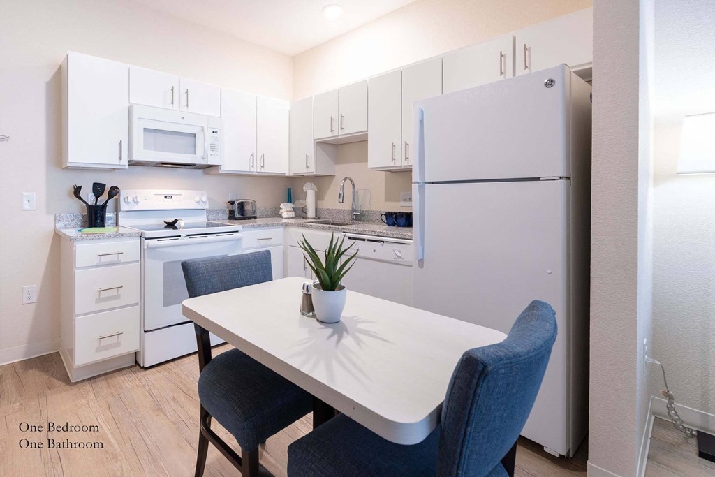 a kitchen with white appliances and a white table with blue chairs at Parks Residential - Richardson, Richardson, 75082
