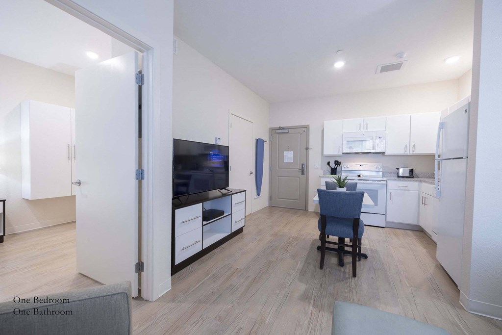 a living room and kitchen with white cabinets and a table with a chair at Parks Residential - Richardson, Richardson
