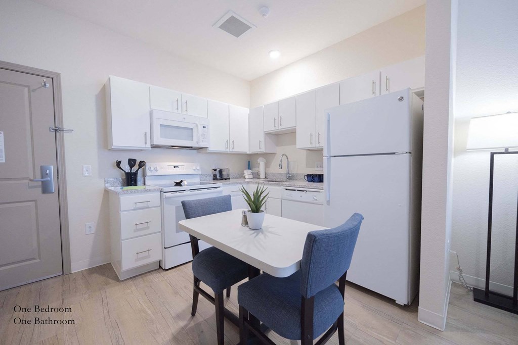 a kitchen with white cabinets and white appliances and a white table with two blue chairs at Parks Residential - Richardson, Texas, 75082