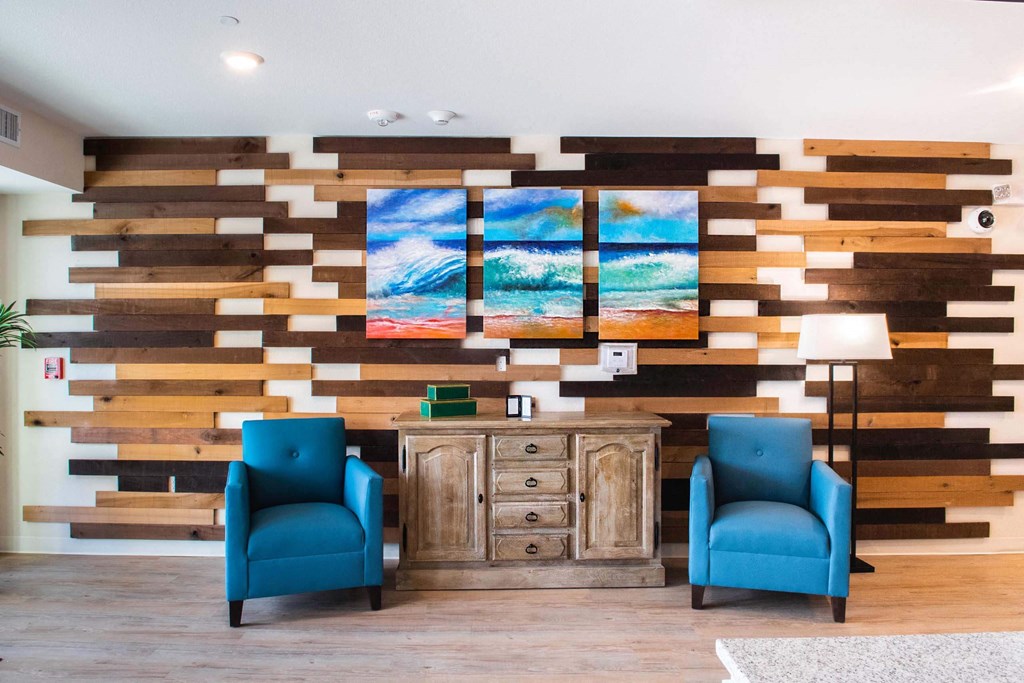 a lobby with two blue chairs and a wall with three paintings on it  at Parks Residential - Richardson, Texas, 75082