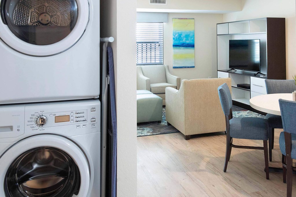 a living room with a washing machine and a kitchen with a table and chairs at Parks Residential - Denver, Centennial Colorado