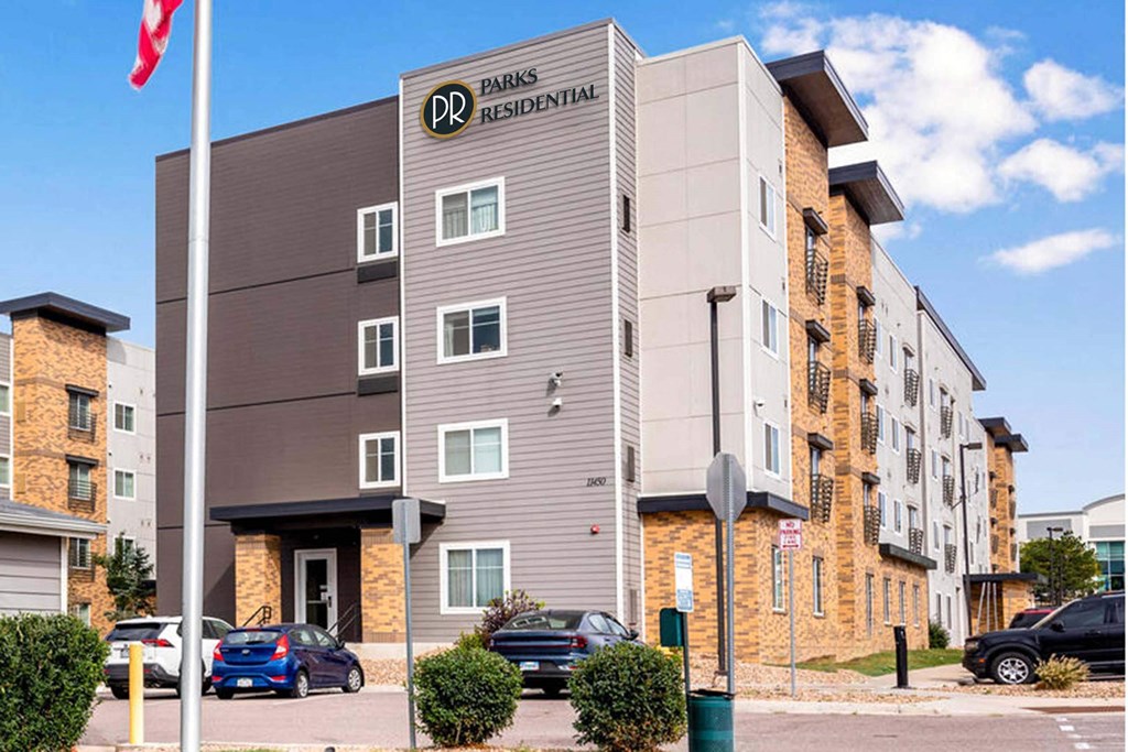 a building with a flag and cars parked in front of it at Parks Residential - Denver, Centennial, CO 80111