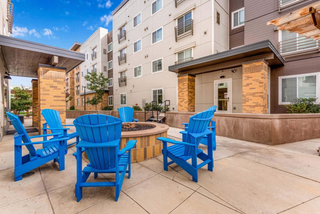 a patio with blue chairs and a fire pit in front of an apartment building at Parks Residential - Denver, Centennial
