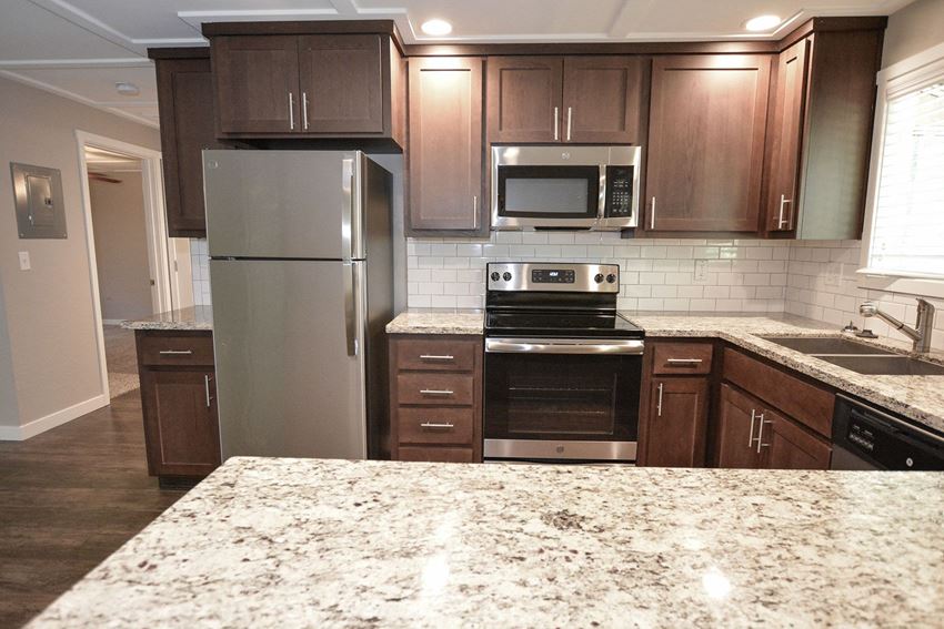 Kitchen Alternate view of kitchen with stone counters, tile backsplash, brown cabinets, stainless appliances, recessed lighting, and wood like flooring - Photo Gallery