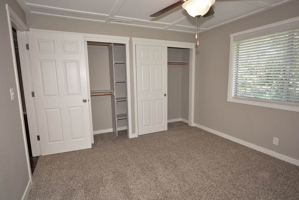 View of bedroom with carpet flooring, sliding door closet with built in shelving, well lit window and ceiling fan