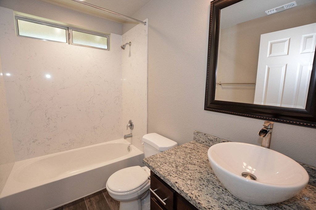 view of bathroom with vessel sink, mirror, toilet, tub shower combo, and well lit window