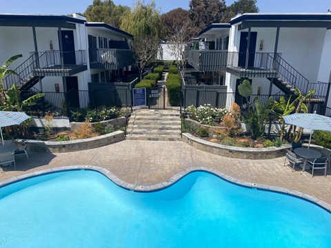A swimming pool in front of a building with a patio and chairs.