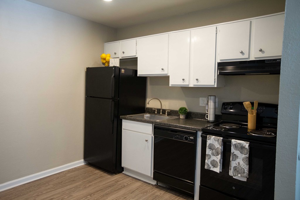 View of kitchen with dark counters, black appliances, and white cabinets with wood look flooring