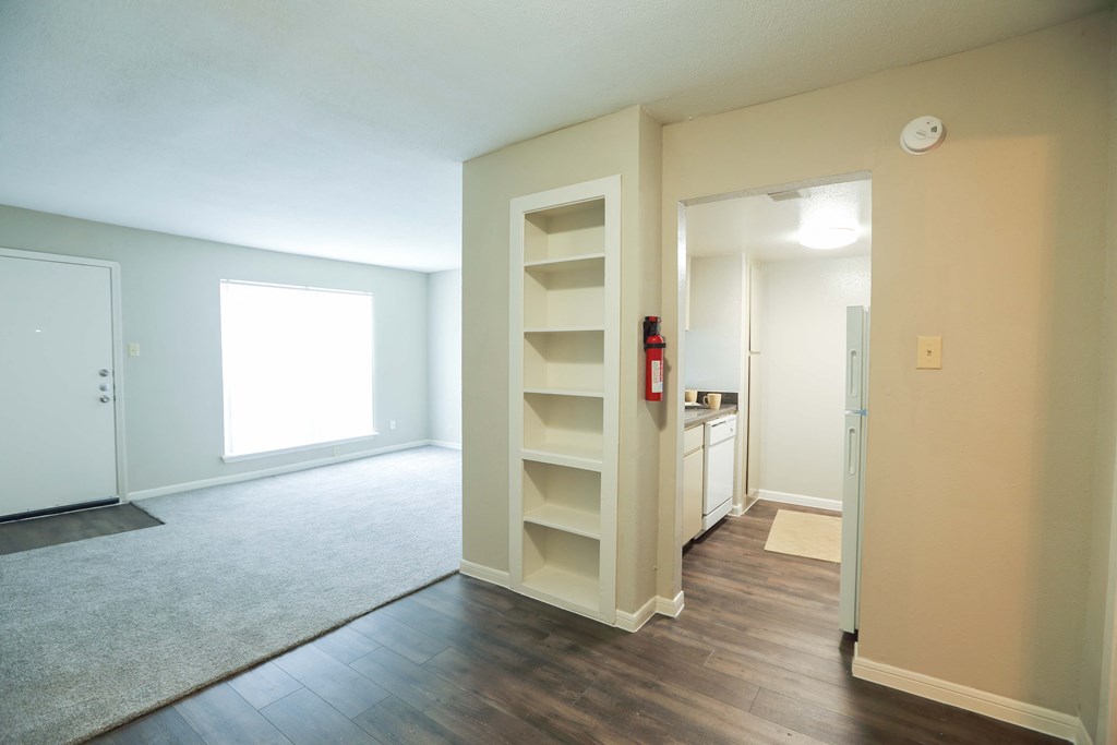 a empty living room with a book shelf and a kitchen