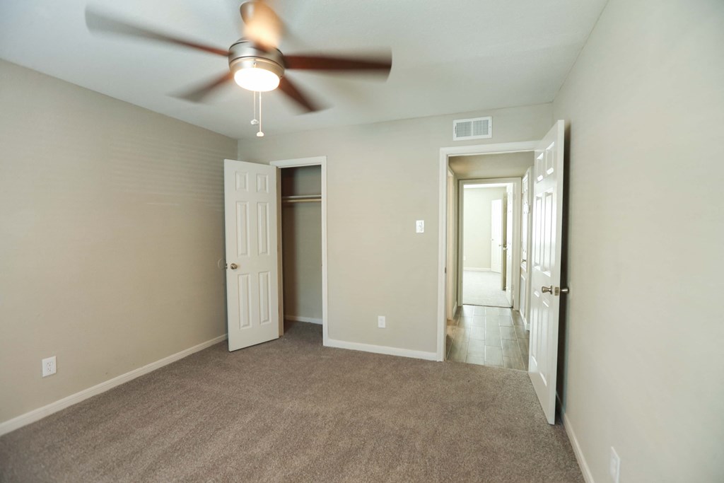 an empty living room with a ceiling fan and a hallway
