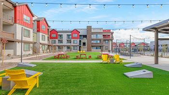 A grassy area with picnic tables and benches in front of apartment buildings.