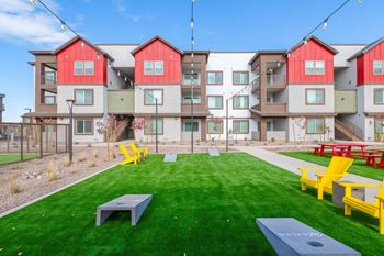 A grassy area in front of apartment buildings with yellow chairs and tables.