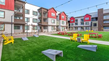 A grassy area with picnic tables and benches in front of apartment buildings.