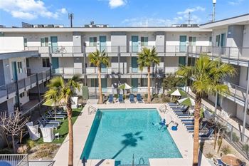 A swimming pool surrounded by palm trees and lounge chairs in front of apartment buildings.