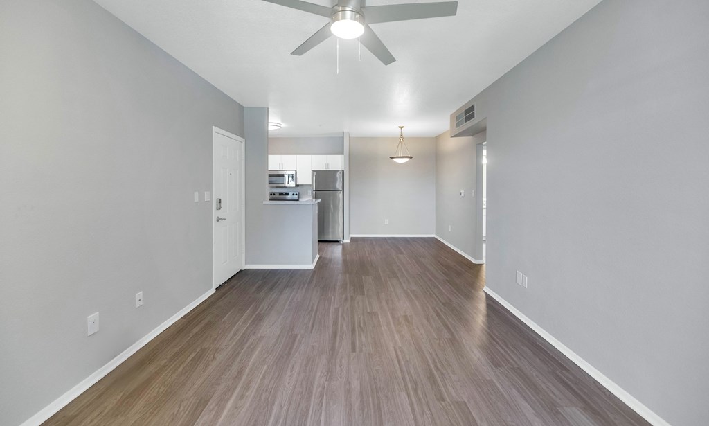 A long hallway with a fan and a kitchen in the distance.