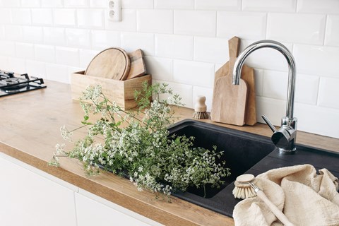 A kitchen sink with a wooden box and a brush on the counter.