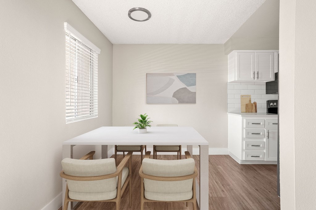 a dining area with a white table and four chairs and a kitchen in the background