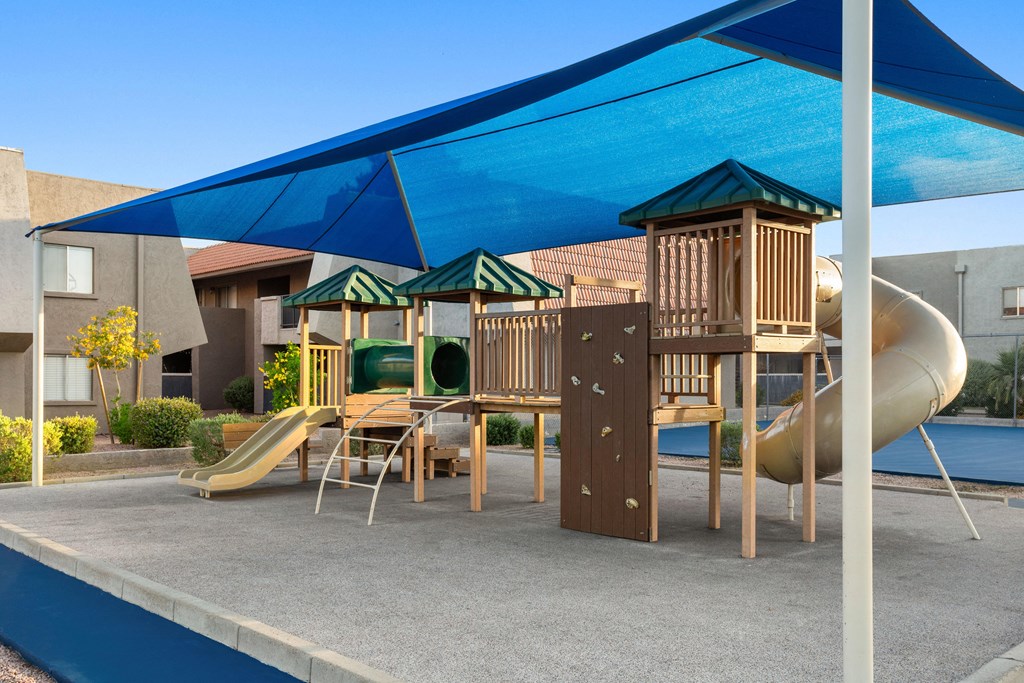 a playground with a slide and a table and chairs under a blue awning