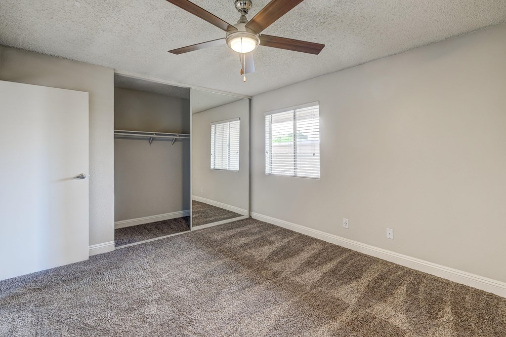 an empty living room with a ceiling fan and a closet
