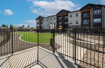 A black metal fence surrounds a playground area in front of apartment buildings.