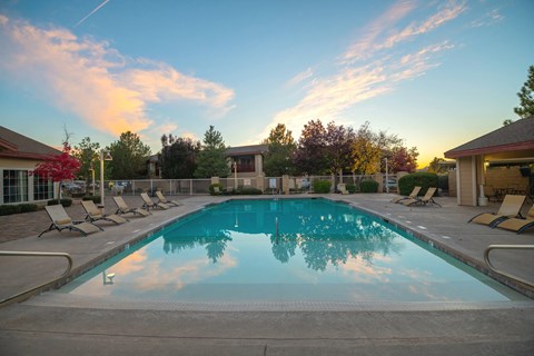 a swimming pool with chairs around it at sunset