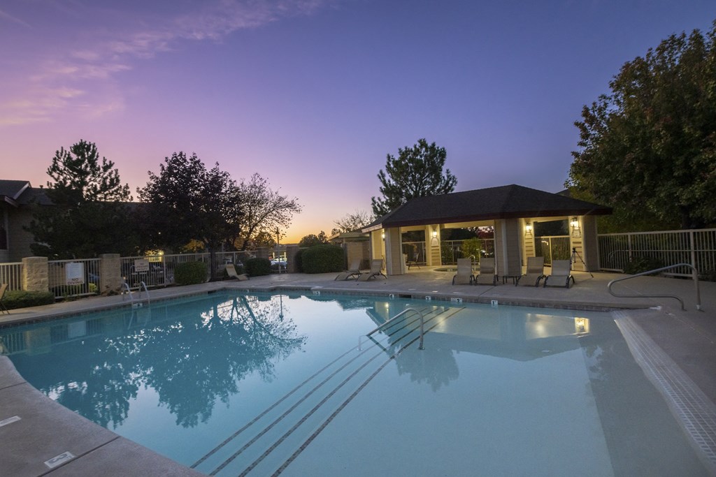 a swimming pool with a pavilion and chairs around it at dusk