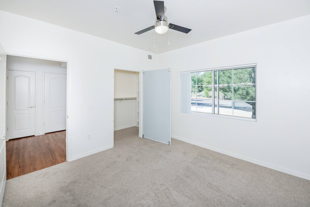 A room with a ceiling fan and a window overlooking a street.