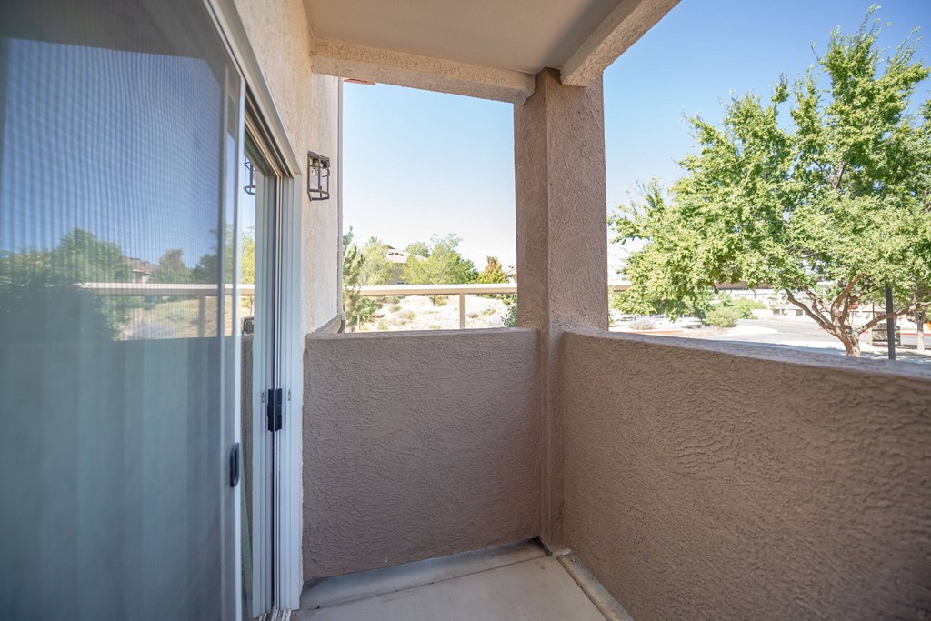 A balcony with a sliding glass door leading to a view of trees and a clear blue sky.