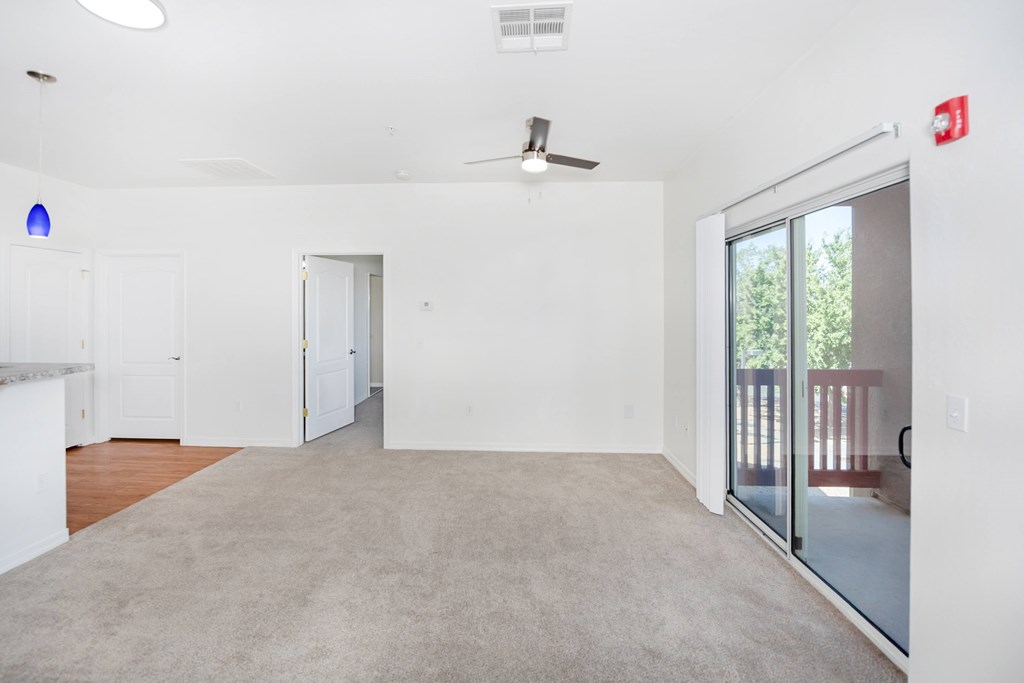 A spacious room with a ceiling fan and sliding glass doors leading to a balcony.