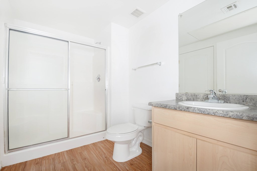 A white toilet sits in a bathroom with a marble counter and a walk-in shower.