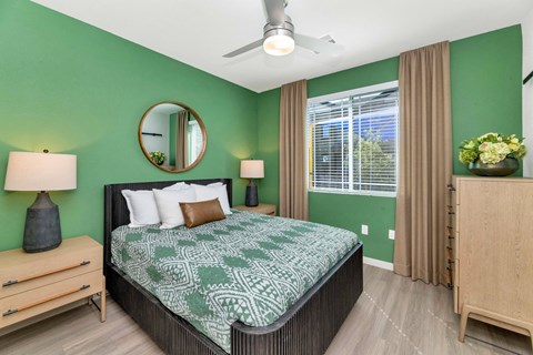 A bedroom with a bed, nightstand, and a mirror on the wall.