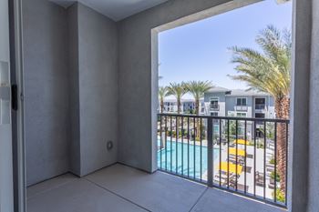 A balcony with a pool and palm trees in the distance.