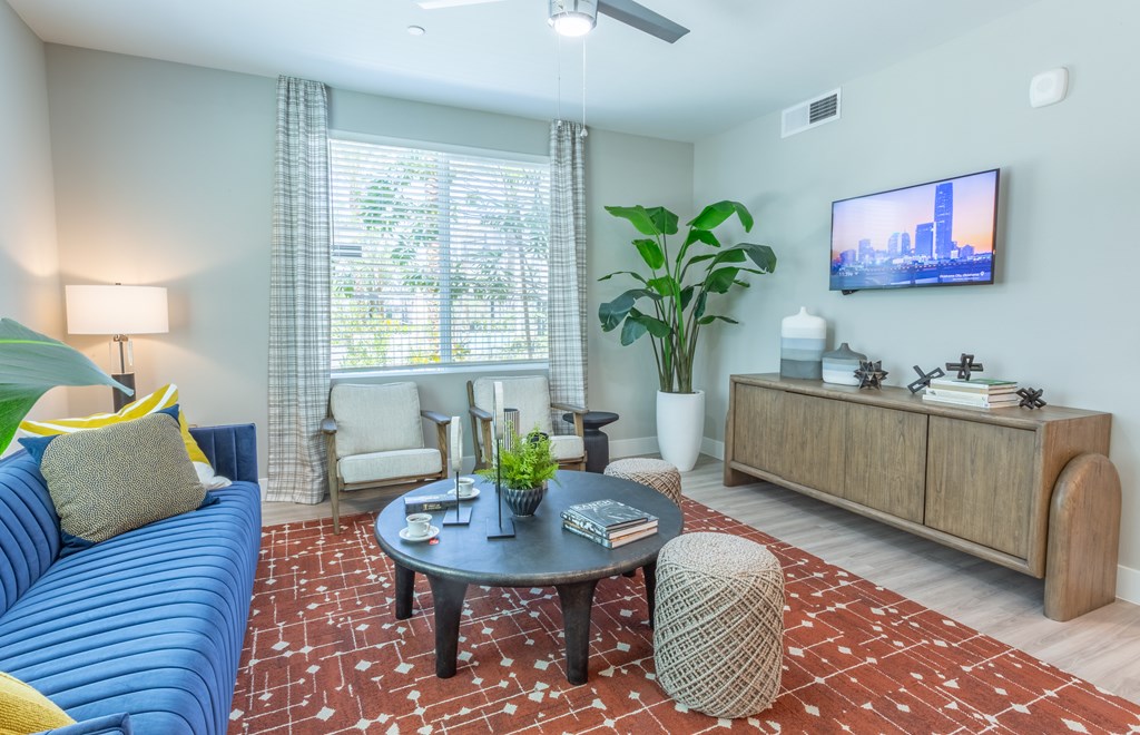 A living room with a blue couch, a coffee table, a TV, and a large window with a view of the city.