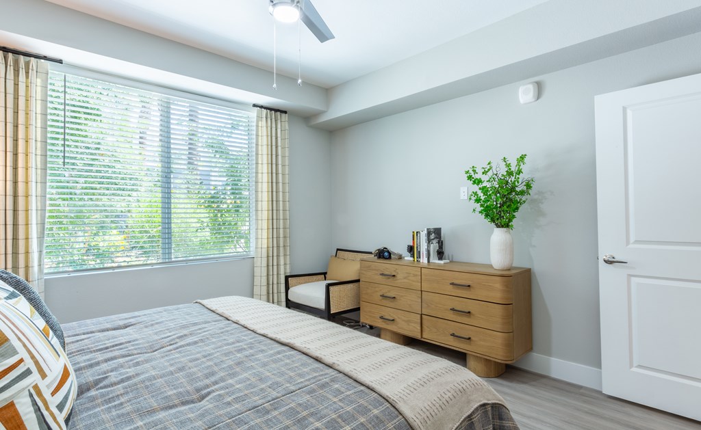 A bedroom with a bed, nightstand, and window with blinds.