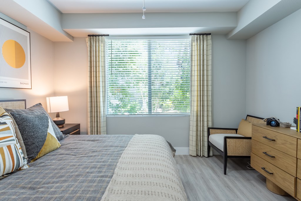 A bedroom with a large bed, a nightstand, and a window with curtains.