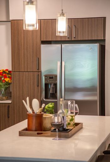 A kitchen with a refrigerator, wooden cabinets, and a tray with utensils and glasses.
