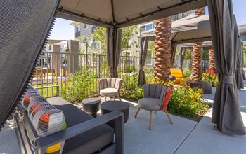 A patio with a grey sofa and a grey chair under a grey umbrella.