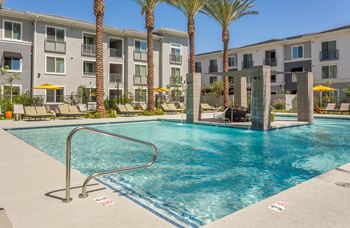 A swimming pool in front of apartment buildings with palm trees.