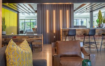 A modern living room with a grey couch, a brown leather chair, and a yellow pillow.