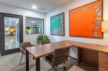 A conference room with a wooden table and chairs, a plant, and two framed pieces of artwork on the wall.