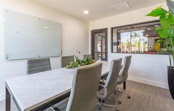 A conference room with a whiteboard, grey chairs, and a table with a plant on it.