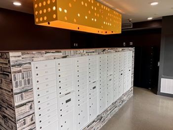 A wall of mailboxes in a room with a yellow light fixture above.