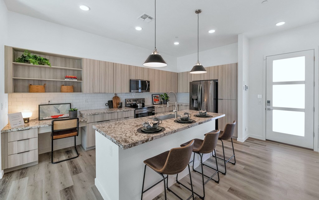 A modern kitchen with a marble countertop and wooden flooring.at Marketside Villas at Verrado, Buckeye, AZ