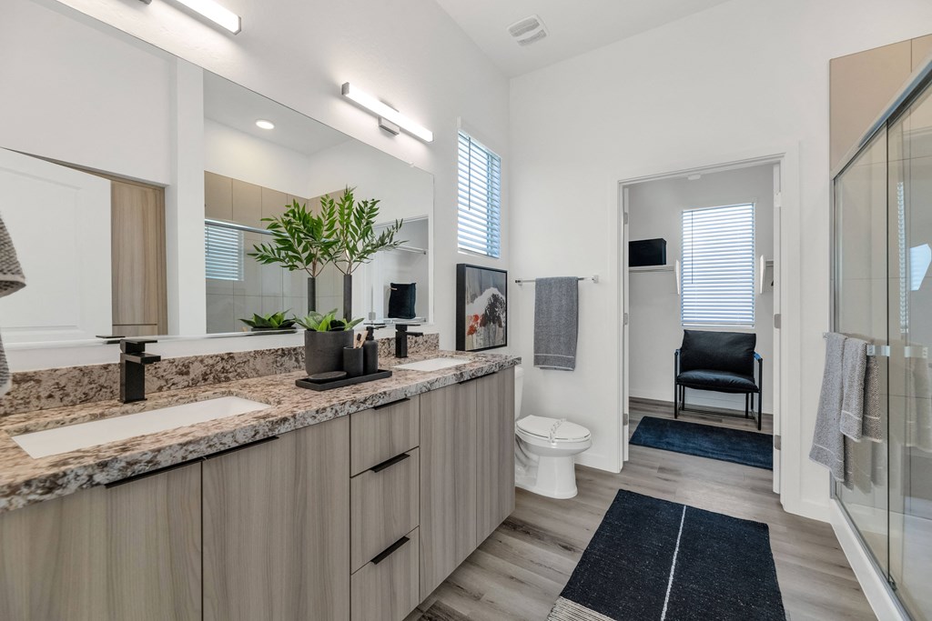 A bathroom with a sink, mirror, toilet, and a chair.at Marketside Villas at Verrado, Buckeye