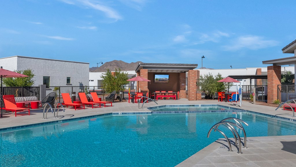 A swimming pool with red chairs and a building in the background.at Marketside Villas at Verrado, Buckeye, 85396